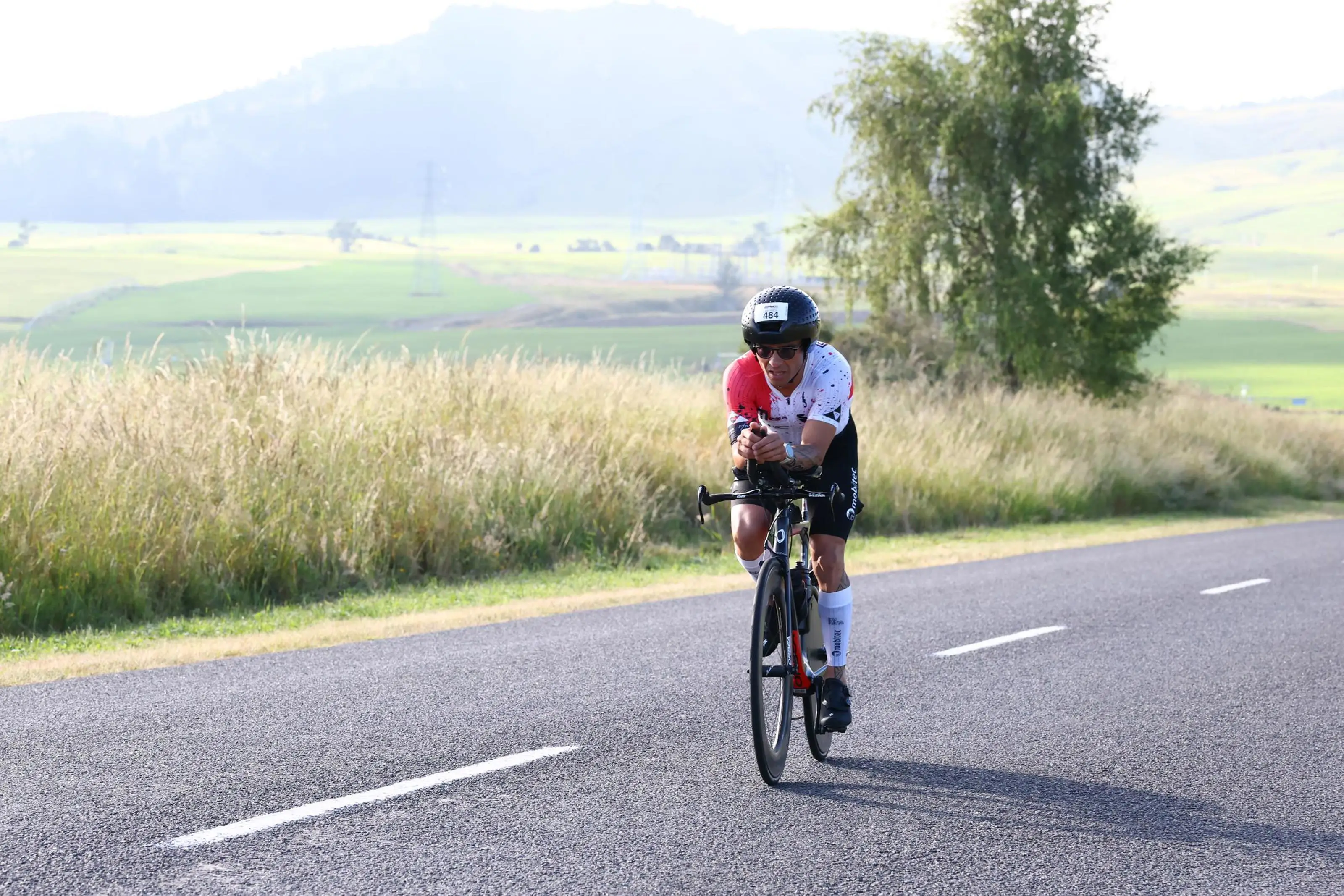 Hermes pedalando na clip em uma estrada aberta entre campos
