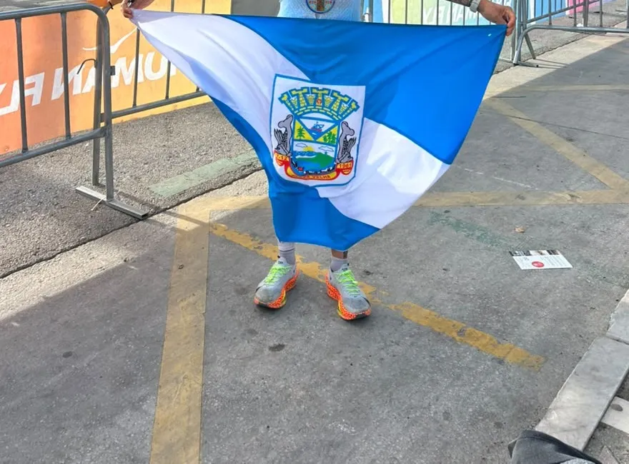 Hermes no Mundial IRONMAN 70.3 em Marbella, com a medalha no peito, segurando a bandeira de Barra Velha
